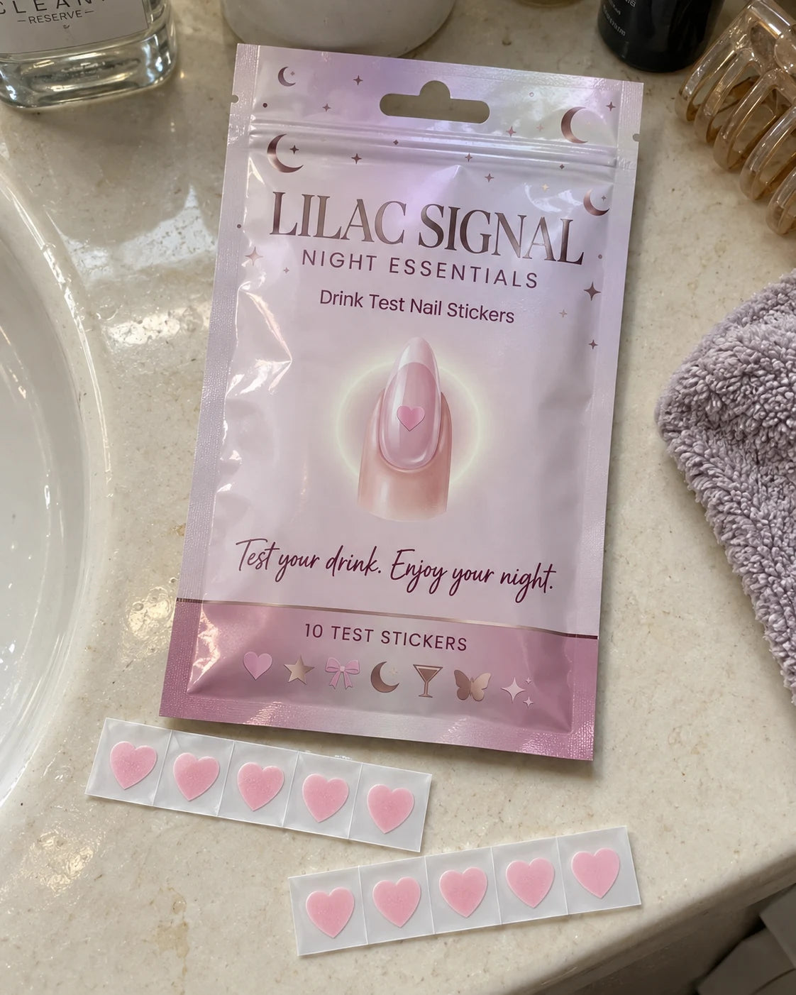 Lilac Signal lilac pouch with two strips of pink heart-shaped nail stickers on a bathroom counter